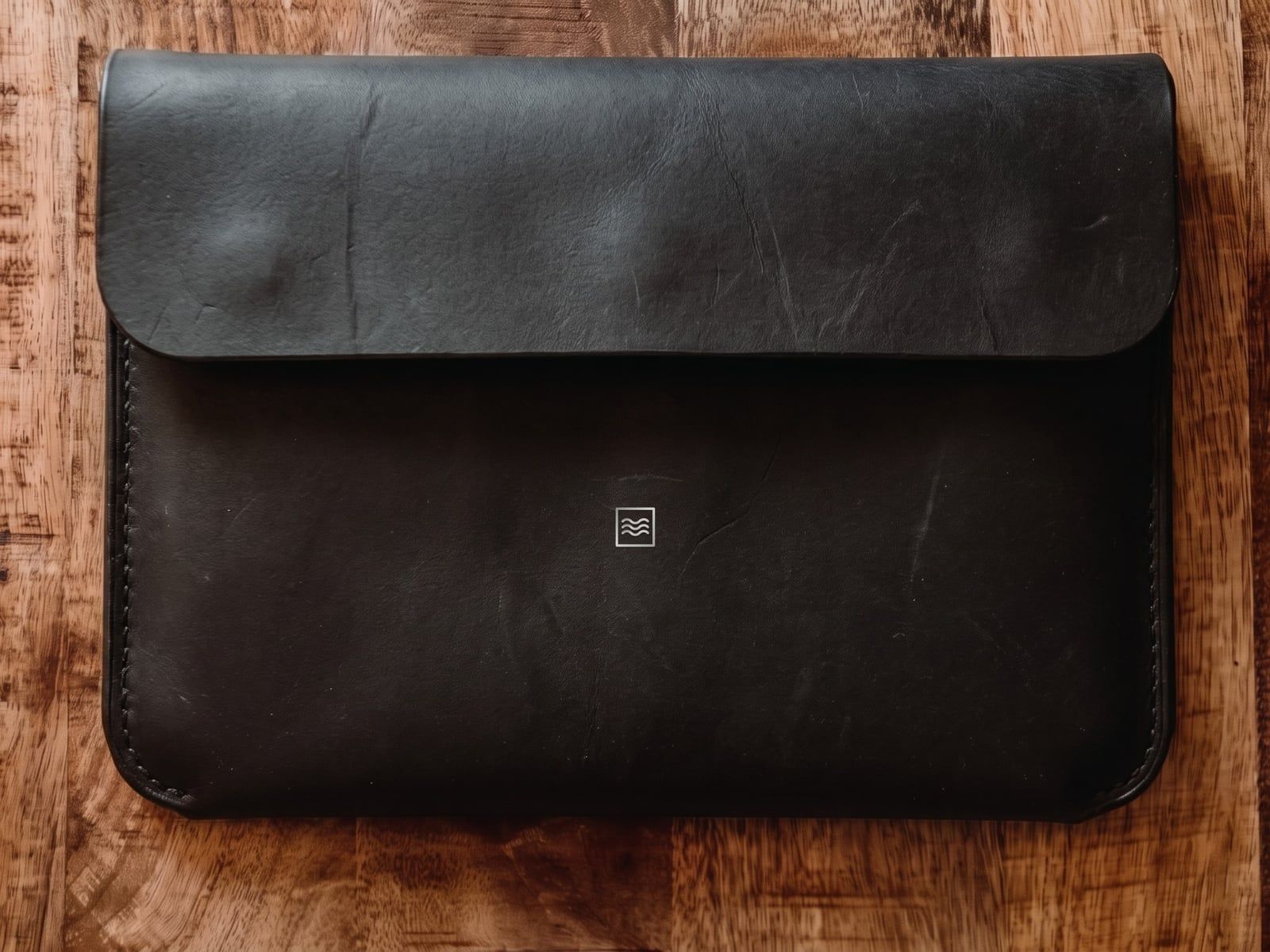 A closed sleeve in black leather with a flap, stitched sides and the Tidemark monogram in silver foil.