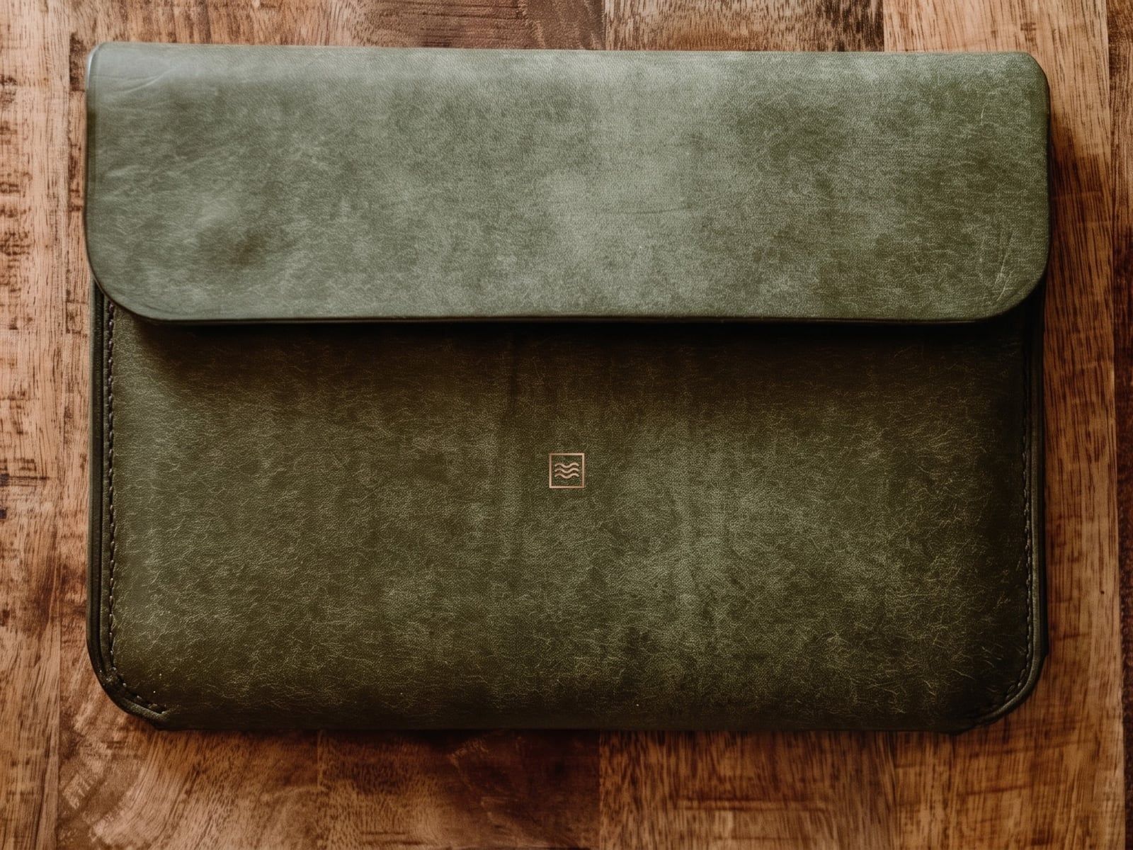 A closed sleeve in olive green leather with a flap, stitched sides and the Tidemark monogram in copper foil.