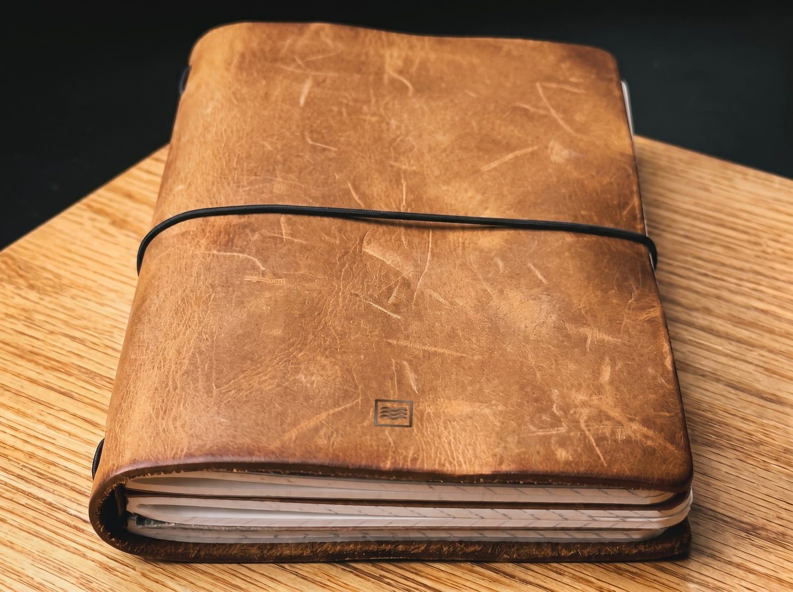 The System: an A6 cover in light crazy horse leather with the Tidemark monogram pressed blind into the leather, an elastic cord and a stack of inserts.